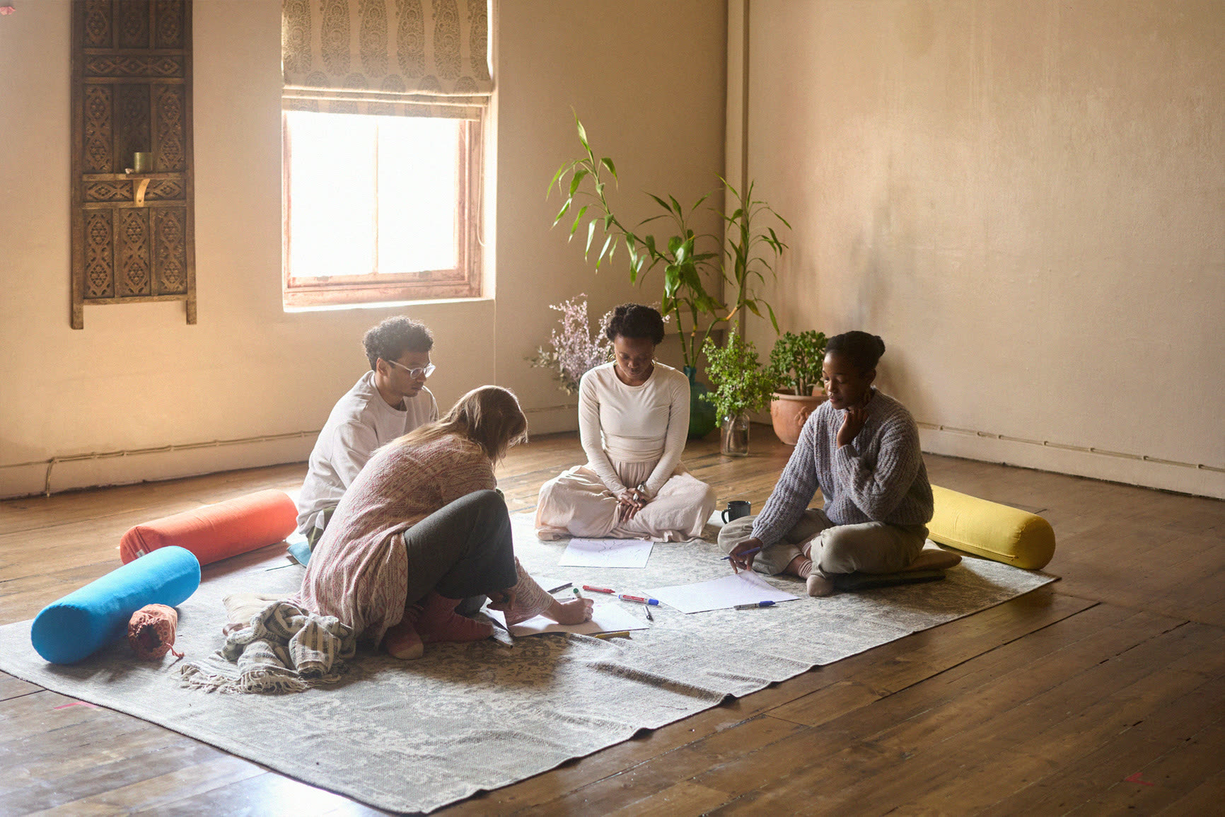 A small group sitting together on a studio floor, working over sheets of paper