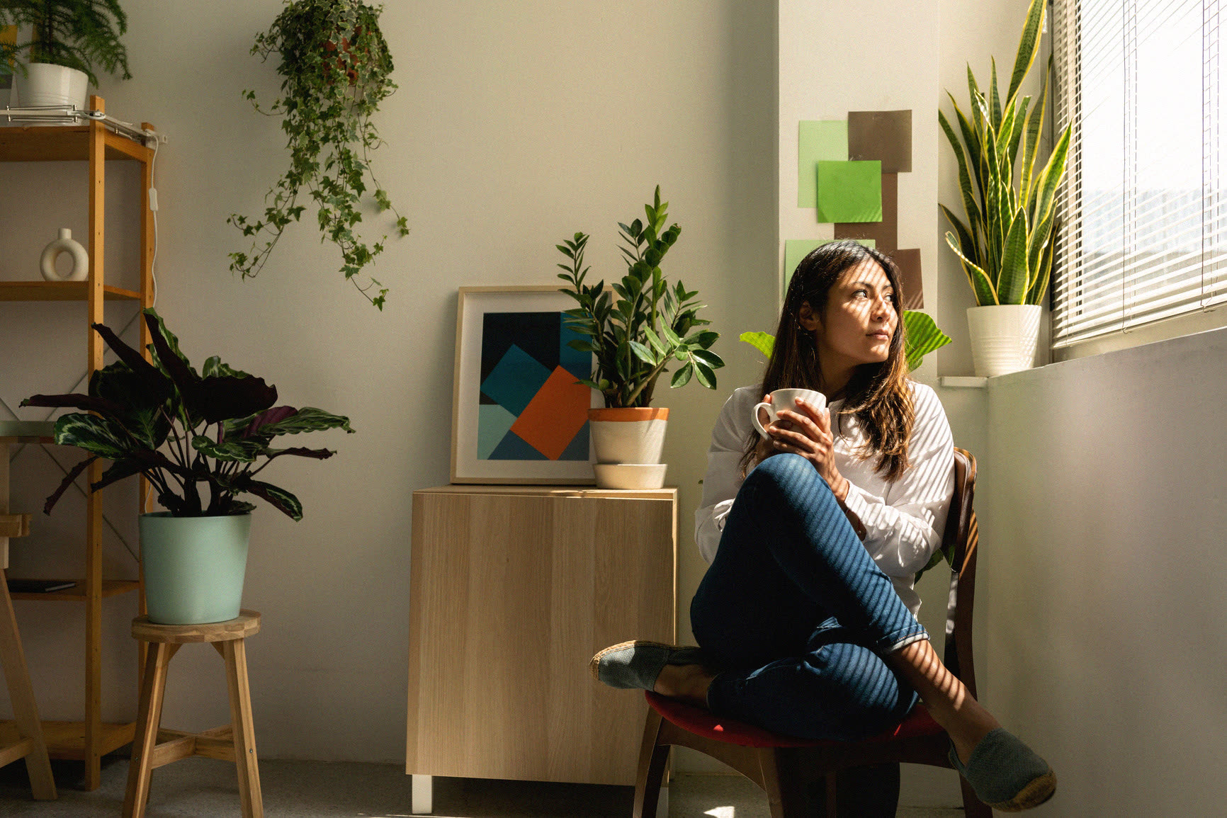 A woman sitting alone with a warm drink beside a sunlit window