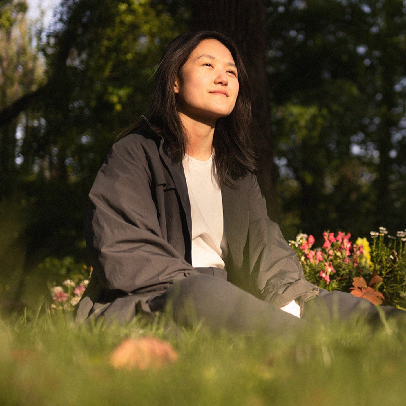 A woman sitting in a meadow, face turned to the late sun